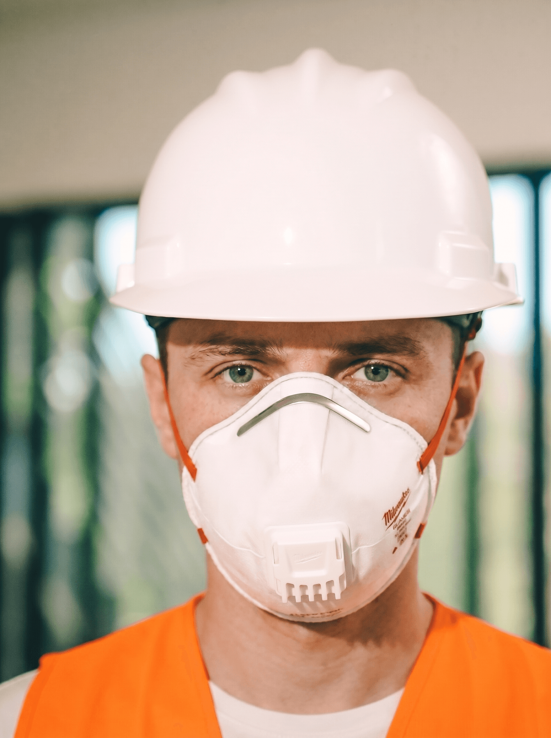 Stavebný pracovník v bielej helme a oranžovej veste s nasadeným respirátorom FFP2